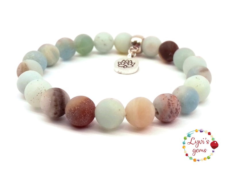 May include: A light green, brown, and white gemstone bracelet with a silver lotus charm. The bracelet is made of round beads and is approximately 7 inches in length.