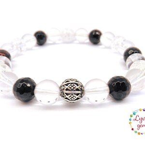 May include: A beaded bracelet featuring clear, black, and silver beads. The bracelet has a mix of faceted black beads, clear quartz, and a decorative silver bead. The bracelet is on a white background.