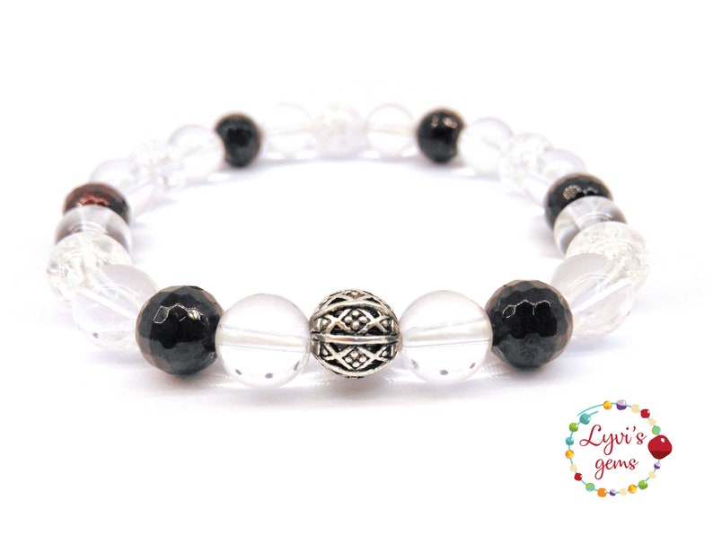 May include: A beaded bracelet featuring clear, black, and silver beads. The bracelet has a mix of faceted black beads, clear quartz, and a decorative silver bead. The bracelet is on a white background.