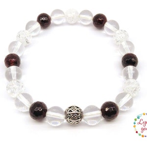 May include: A beaded bracelet featuring clear, faceted, and dark red gemstones. The bracelet includes clear, round beads and a decorative silver bead. The bracelet is on a white background. The image also includes a logo with the text "Lyvi's gems".
