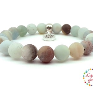 May include: A light blue, brown, and white gemstone bracelet with a silver lotus charm. The bracelet is made of round beads and is approximately 7 inches in length.