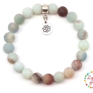 May include: A light blue and brown gemstone bracelet with a silver lotus charm. The bracelet is made of round beads and is approximately 7 inches in length.