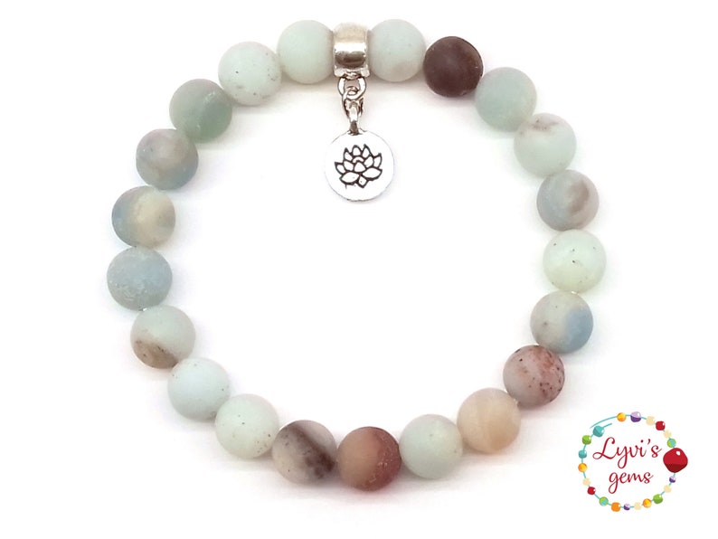 May include: A light blue and brown gemstone bracelet with a silver lotus charm. The bracelet is made of round beads and is approximately 7 inches in length.