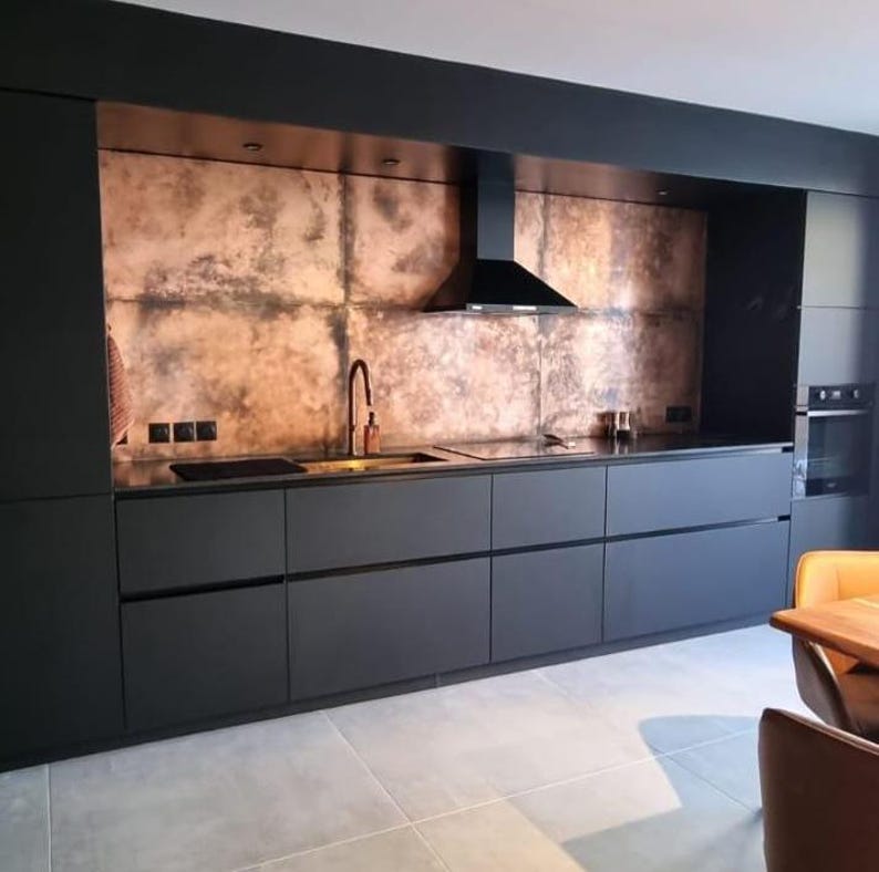 Open plan kitchen with matte black cabinets and large copper splashback wall