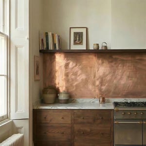 May include: A kitchen interior featuring a copper backsplash, wooden cabinets, and a marble countertop. A stainless steel stove is on the right. A shelf above holds books, artwork, and ceramic pieces. The room has a warm, inviting atmosphere.