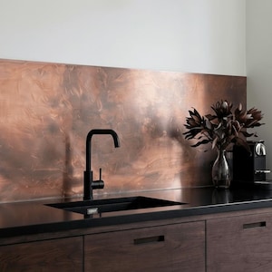 May include: A modern kitchen design featuring a black faucet and sink set against a copper backsplash. Dark wooden cabinets and a vase of dark flowers add to the contemporary aesthetic. A coffee machine is visible on the countertop.