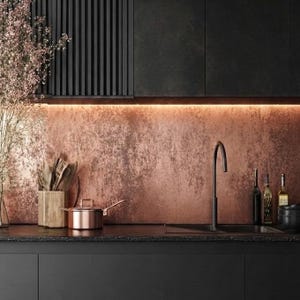 May include: A modern kitchen design featuring a copper backsplash, black cabinets, and a black sink with a curved faucet. A copper saucepan sits on the countertop, with bottles and a wooden utensil holder nearby. Soft lighting illuminates the space.