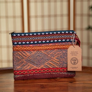 May include: A colorful woven clutch bag with a zipper closure. The bag has a brown paper tag attached with the text "Handcrafted Treasures from the Andes" and a logo.