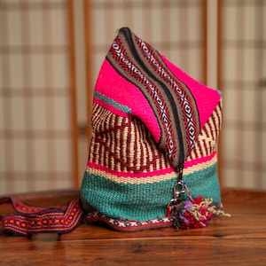 Op de afbeelding: Een kleurrijke geweven tas met een roze, groene, bruine en beige print. De tas heeft een ritssluiting en een kwast.
