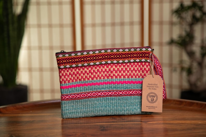 May include: A teal, pink, red, and white woven clutch with a brown tag that reads "Handcrafted Textiles from The Andes".