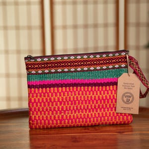 May include: A colorful woven clutch bag with a zipper closure and a brown tag that reads "Handcrafted Treasures from The Andes".