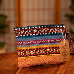 May include: A colorful woven clutch bag with a brown leather strap and a tag that reads "Handmade Treasures from the Andes".