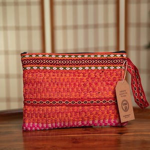 May include: A red, orange, and pink woven clutch bag with a black zipper and a brown tag that says "Handmade from The Andes".