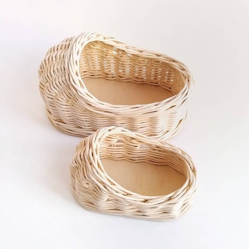 May include: Two woven wicker baskets, one larger than the other, both with a light beige color. The baskets are oval shaped and have a smooth, woven texture.