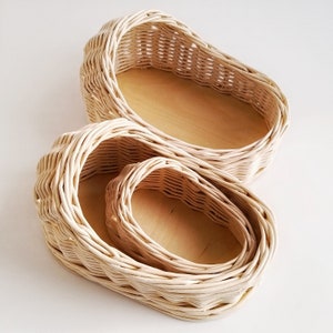 May include: Three woven wicker baskets, nested inside each other, with a natural wood finish. The baskets are oval shaped and have a smooth, natural texture.