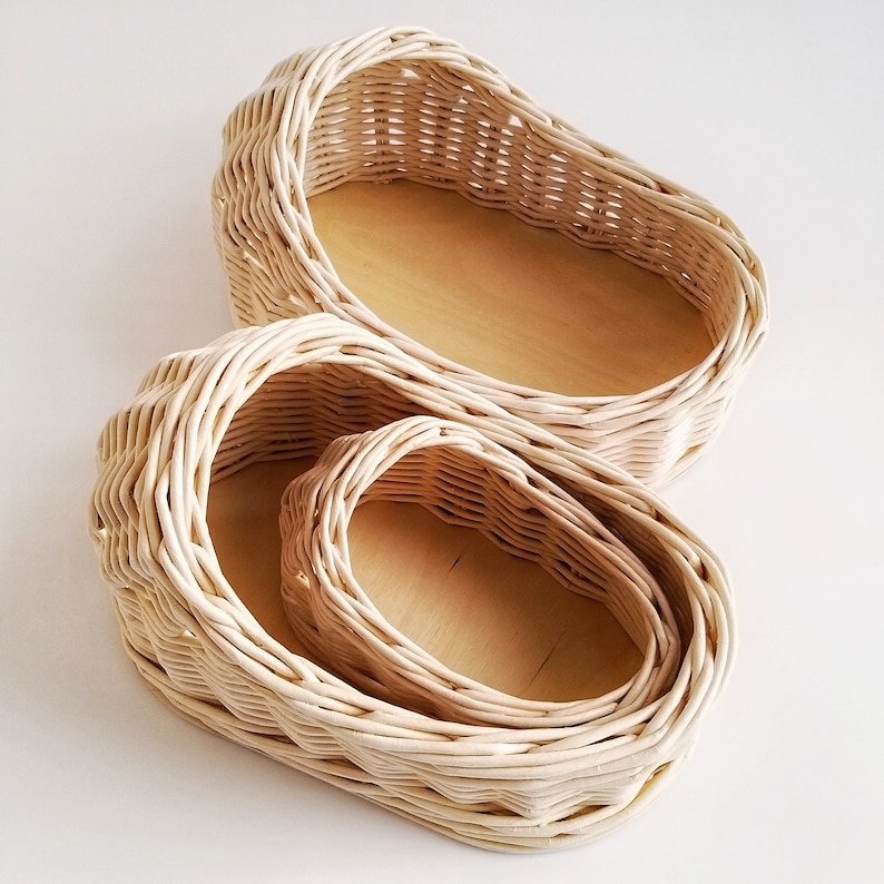 May include: Three woven wicker baskets, nested inside each other, with a natural wood finish. The baskets are oval shaped and have a smooth, natural texture.