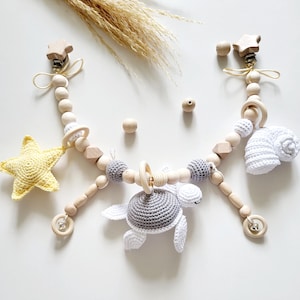 Puede incluir: Un juguete de madera para bebé con una estrella, una tortuga, una concha y un anillo. El juguete está hecho de cuentas de madera natural y tiene un clip para sujetarlo a un cochecito o cuna.