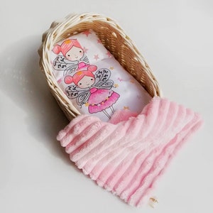 May include: A white wicker doll crib with a pink and white fairy-themed bedding set and a pink plush blanket.