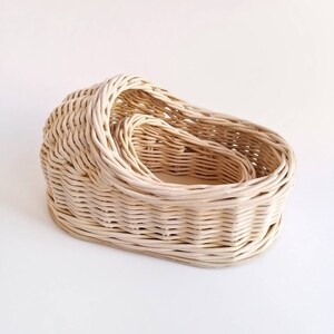 May include: A set of three woven wicker baskets, nested inside each other. The baskets are oval shaped and have a natural, light brown color.