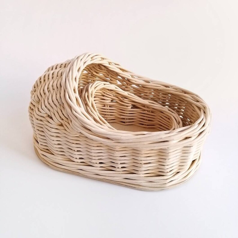 May include: A set of three woven wicker baskets, nested inside each other. The baskets are oval shaped and have a natural, light brown color.