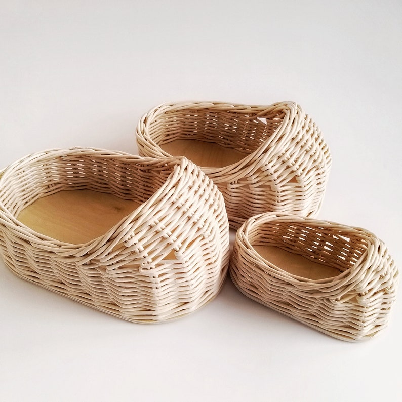 May include: Three woven wicker baskets in various sizes, all in a light beige color. The baskets are oval shaped and have a natural wood base.