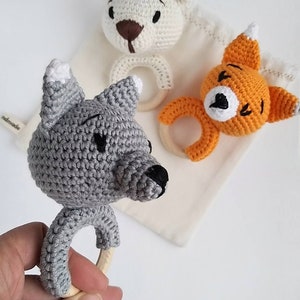 May include: Three crocheted animal teethers with wooden rings. The teethers are a gray wolf, a white bear, and an orange fox. The teethers are on a white background.