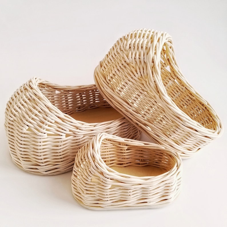 May include: Three white wicker baskets of varying sizes. The baskets are woven in a tight pattern and have a natural, rustic look.