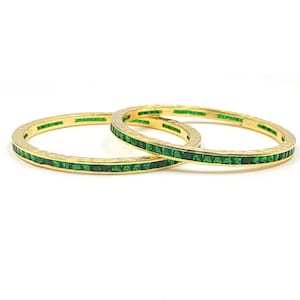 Può includere: Due bracciali rigidi circolari color oro caratterizzati da un'incastonatura a binario continua di piccole pietre quadrate verde smeraldo. La superficie metallica dei bracciali presenta una finitura martellata e testurizzata.