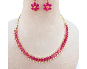 May include: A gold-toned jewelry set featuring a necklace and matching earrings. The necklace and earrings are adorned with vibrant pink teardrop-shaped stones and small white pearls. The earrings have a flower design.