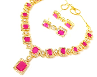 May include: A gold-toned jewelry set featuring a necklace and matching earrings. The necklace and earrings have a repeating pattern of square, hot pink gemstones, each framed by a border of small, clear crystals. The set is displayed on a white background.