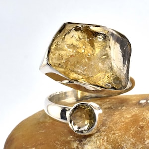 May include: A silver ring featuring a large, faceted, yellow citrine gemstone. The ring has a twisted band and a smaller citrine gemstone on the side.