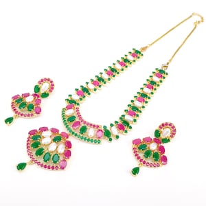 May include: A gold-toned necklace and matching earrings set. The necklace and earrings feature a pattern of alternating green, pink, and white gemstones. The earrings have a teardrop-shaped green gemstone at the bottom.