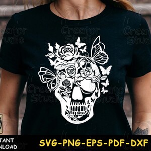 May include: A black t-shirt with a white design of a skull with flowers and butterflies. The design is intricate and detailed, with the skull's eyes replaced by flowers and butterflies.