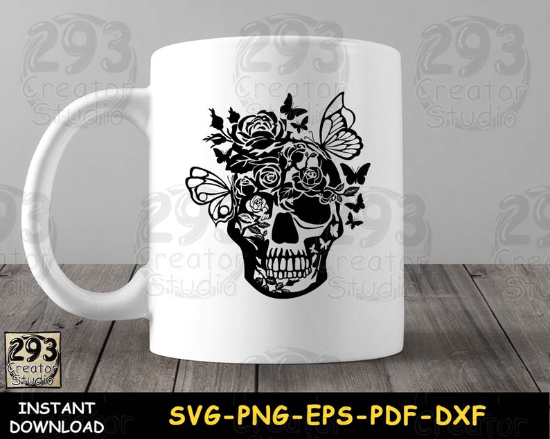 May include: White ceramic mug with a black silhouette of a skull with flowers and butterflies on the front. The mug is on a wooden surface.