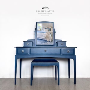 May include: A navy blue vanity table with a matching stool, featuring a central rectangular mirror, three drawers with decorative knobs, and two small side compartments. The text GRACIE'S ATTIC BESPOKE PAINTED FURNITURE is visible above the mirror.