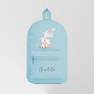 Può includere: Zaino azzurro con tasca frontale con cerniera e maniglia superiore. Lo zaino presenta la lettera "C" rosa con un'illustrazione di giraffa ed elefante e il nome "Charlotte" in corsivo.