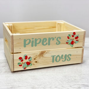 Puede incluir: Una caja de madera con las palabras "Piper's Toys" y un diseño de huella de pata. La huella de pata está decorada con un patrón floral en tonos rojos y verdes.