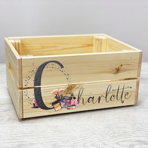 May include: A wooden crate with a personalized design featuring the letter "C" and the name "Charlotte". The design includes a black and white illustration of makeup brushes, lipstick, and eyeshadow palettes.
