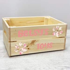 Puede incluir: Una caja de madera con un diseño de huella de pata rosa con flores. La caja está etiquetada como "Betsy's Toys".