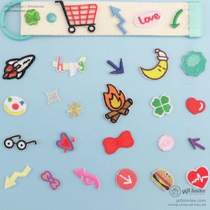 May include: A collection of colorful embroidered patches with various designs, including a shopping cart, arrows, a rocket, a crescent moon, a campfire, and the word "Love". The patches are on a light blue background.