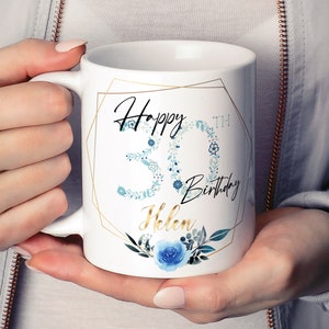 Może przedstawiać: Biały kubek ceramiczny z złotą geometryczną ramką i niebieskim wzorem kwiatowym. Na kubku nadrukowany jest tekst "Happy 30th Birthday Helen".