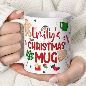 May include: White ceramic mug with a colourful Christmas design. The mug has the text "Emily's Christmas Mug" in red and green lettering.