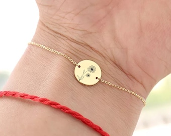 May include: A gold chain bracelet with a round charm featuring a delicate floral design. The charm is engraved with a small flower and stem.
