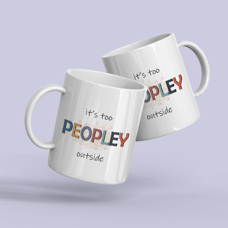 May include: Two white ceramic mugs with the text "it's too PEOPLEY outside" in colorful letters. The mugs have a curved handle and are set against a light purple background.