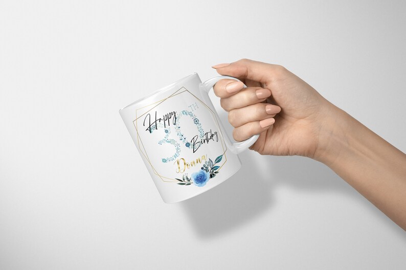 Może przedstawiać: Biały kubek ceramiczny z złotą geometryczną ramką i niebieskim wzorem kwiatowym. Kubek ma napis "Happy 30th Birthday Donna".