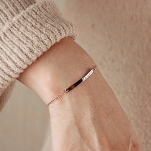 May include: A rose gold chain bracelet with a thin, rectangular bar charm engraved with the name "MEGAN".