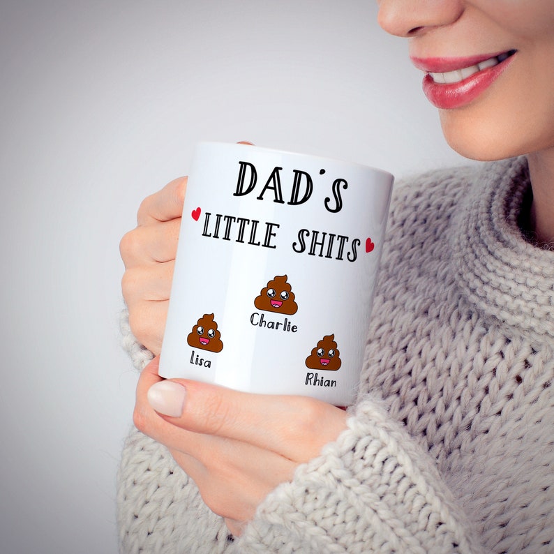 May include: A white ceramic mug featuring the black text DAD'S LITTLE SHITS with two small red hearts. Below the text are three brown cartoon poop emojis with smiling faces, each labeled with the names Lisa, Charlie, and Rhian in black.