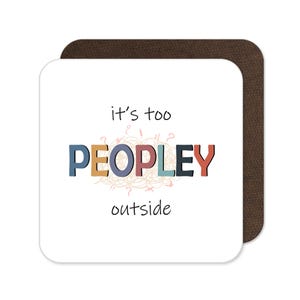 May include: A square white coaster with the text "it's too PEOPLEY outside" in black, blue, orange, and red. The word "PEOPLE" is in colorful block letters. The coaster is on top of a brown square coaster.