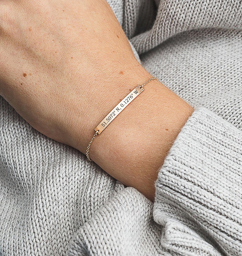 May include: Gold bar bracelet with a delicate chain and engraved coordinates: 51.5072 N 0.1276 W.
