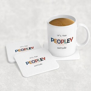 May include: A white ceramic mug filled with coffee and two matching square coasters. The mug and coasters feature the text "it's too PEOPLEY outside" in colorful letters. The mug sits on a white coaster.